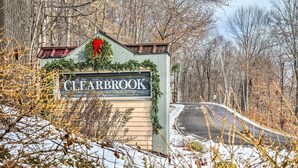 Placa indicando 'Clearbrook', com uma grinalda e guirlanda, rodeada por árvores e neve.