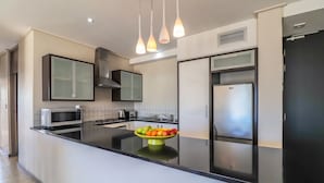 Une cuisine moderne dotée d’un îlot central, d’appareils électroménagers en acier inoxydable et de luminaires suspendus.