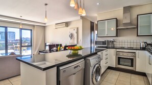 Cuisine moderne équipée d’un lave-vaisselle, d’un lave-linge et d’un four. Une grande fenêtre offre une vue sur la ville.