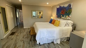 Een slaapkamer met een groot bed, een spiegel, een kleurrijk abstract schilderij en een houten vloer.