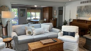 Een woonkamer met een grijze bank, een witte fauteuil, een houten salontafel en een piano.