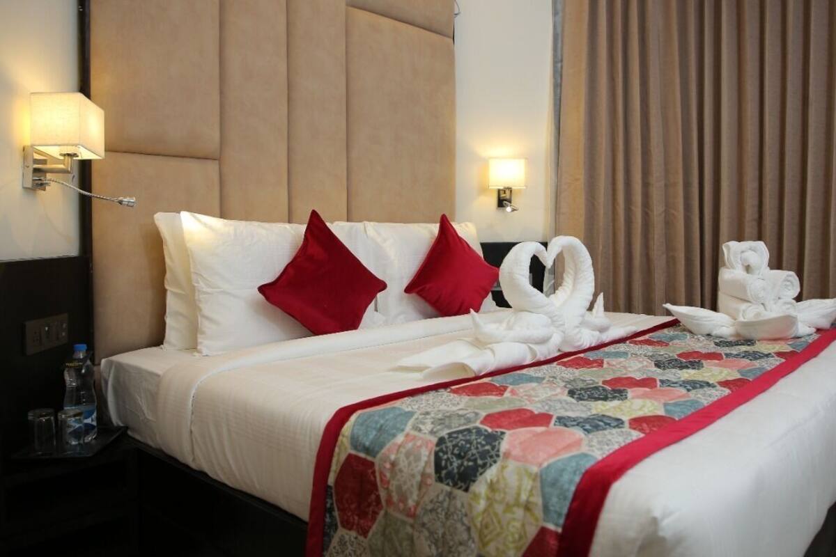 A hotel room with a bed, two wall-mounted lamps, a water bottle, and a quilted bedspread.