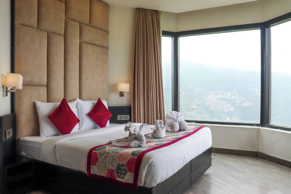 A hotel room with a large bed, a view of the city, and a window with curtains.