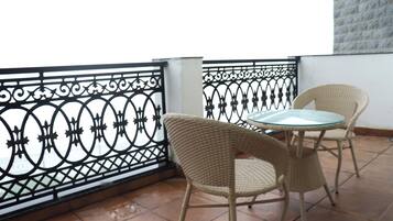A balcony with a wrought iron railing, two wicker chairs, and a glass table.