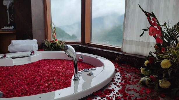 Une salle de bain avec une baignoire remplie de pétales de roses, une fenêtre donnant sur les montagnes et un bouquet de fleurs posé sur le rebord de la fenêtre.