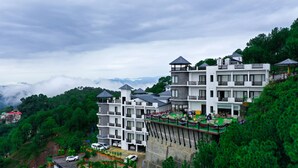 Un hôtel à plusieurs étages, doté de balcons et offrant une vue sur la forêt et les montagnes environnantes.