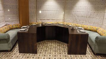 A conference room with a curved dark wood table, light grey sofas with floral upholstery, and patterned floor tiles.