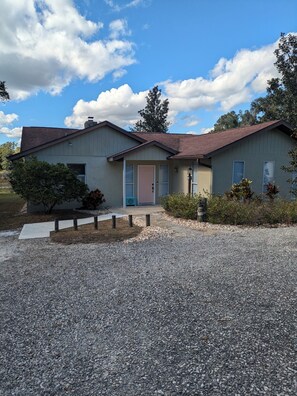 A two-story house with a gravel driveway, a front porch, and a small garden area. - Waterfront lake home w/  fishing, boating, & water activities! (Inverness)