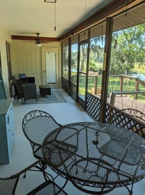 A covered patio with a table and chairs, a view of a garden, and a wooden deck. - Waterfront lake home w/  fishing, boating, & water activities! (Inverness)