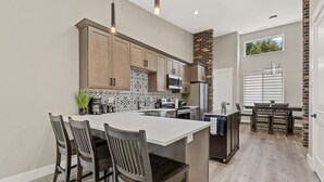 A modern kitchen with a central island, wooden cabinets, and a dining area with a table and chairs. - "The Ponderosa"-Gathering Tree's Deluxe Group Stay with private KING suites (Flagstaff)