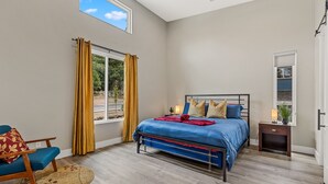 A bedroom with a bed, a chair, a nightstand, and a window with curtains. - "The Ponderosa"-Gathering Tree's Deluxe Group Stay with private KING suites (Flagstaff)