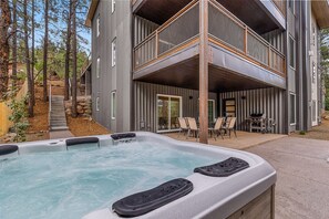 Ein Whirlpool mit einer Holzterrasse, ein zweistöckiges Gebäude mit einem Balkon und Gartenmöbel.