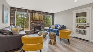 A modern living room with a fireplace, leather sofa, yellow chairs, and large windows. - "The Ponderosa"-Gathering Tree's Deluxe Group Stay with private KING suites (Flagstaff)