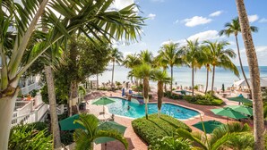A pool area with palm trees, lounge chairs, and umbrellas.