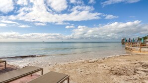 A beach with clear skies, calm water, and a wooden pier with umbrellas.
