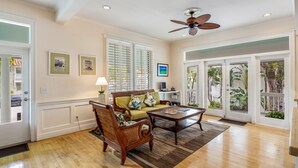 A spacious living room with hardwood flooring, a wooden sofa set, a coffee table, and a ceiling fan.