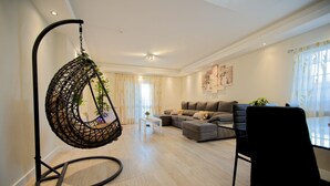 A living room with a hanging chair, a sofa set, and a dining table. - Holiday Home Villa As Cumadres with Mountain View, Pool, Garden & Wi-Fi (Azeitão)