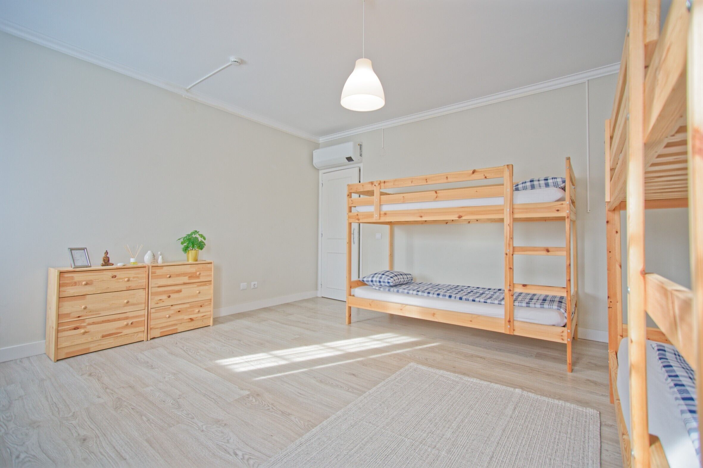 Ein Zimmer mit Etagenbett, Holzkommode und einer Pendelleuchte.