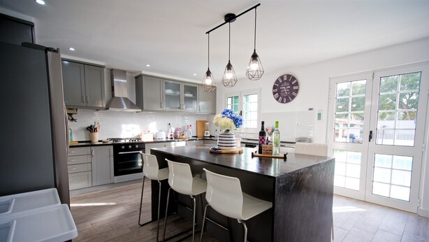A modern kitchen with a large island, bar stools, stainless steel appliances, and pendant lighting. - Holiday Home Villa As Cumadres with Mountain View, Pool, Garden & Wi-Fi (Azeitão)