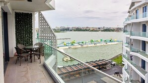 Un balcón con vista a un río, un área de comedor con sillas y un paisaje urbano al fondo.