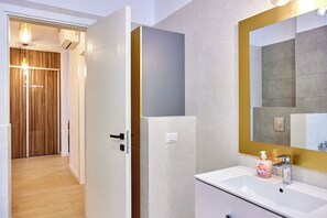 A modern bathroom with a white sink, a large mirror, and a wooden door leading to a hallway. - Apartamente Exterior (Constanta)