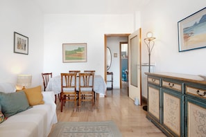 A room with a sofa, dining table, chairs, a cabinet, and artwork on the walls.