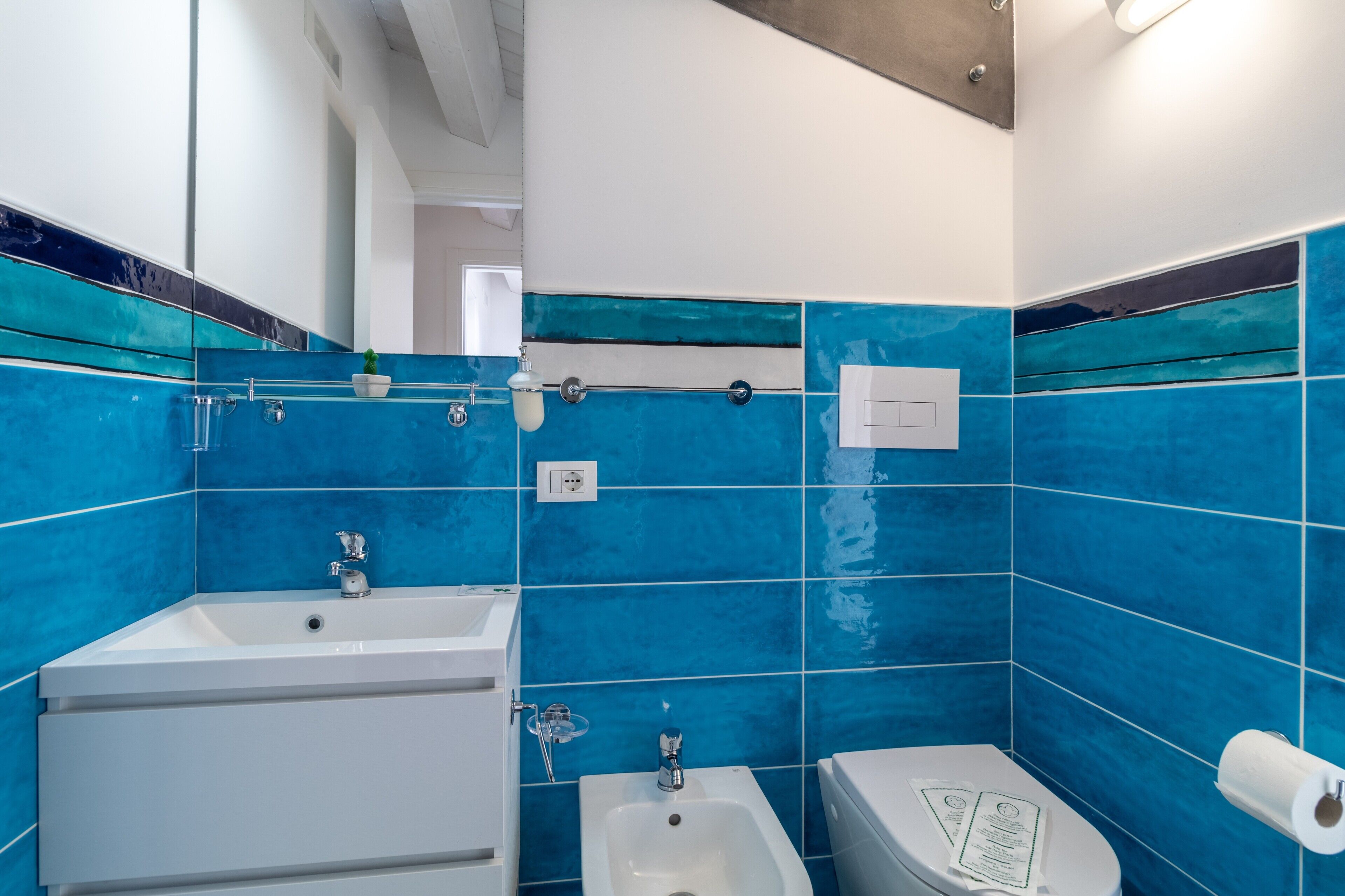 Une salle de bain avec des carreaux bleus, un lavabo, un bidet et des toilettes.