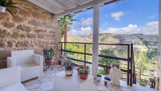 Un balcon agrémenté de meubles en osier peints en blanc, de plantes en pot et offrant une vue sur un paysage montagneux.