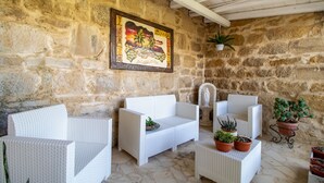 Une pièce aux murs de pierre, meublée de meubles en osier peints en blanc, avec un tableau et des plantes en pot.