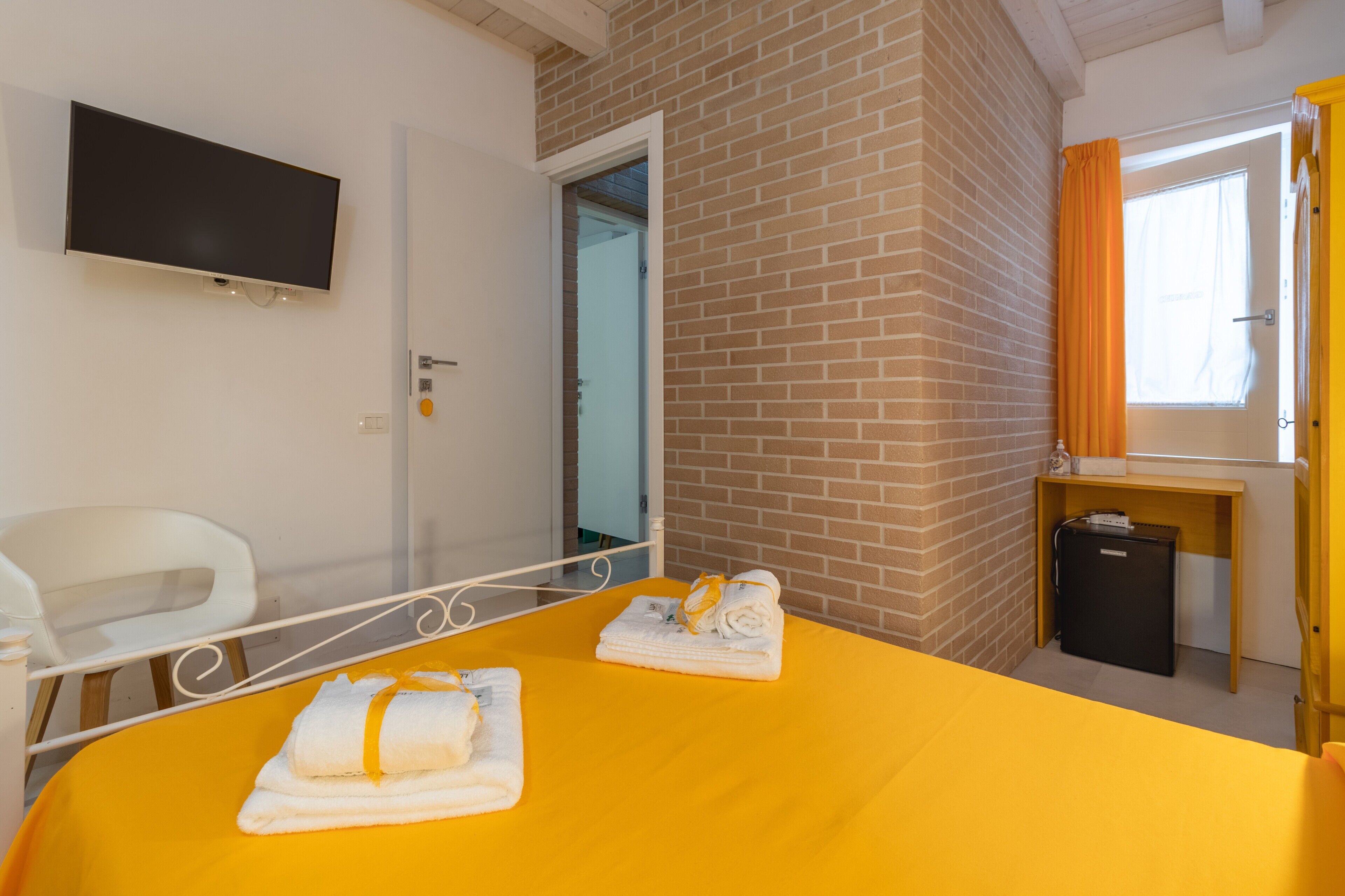 Ein Hotelzimmer mit Bett, Fernseher, Schreibtisch, Stuhl und einem Fenster mit Vorhängen.