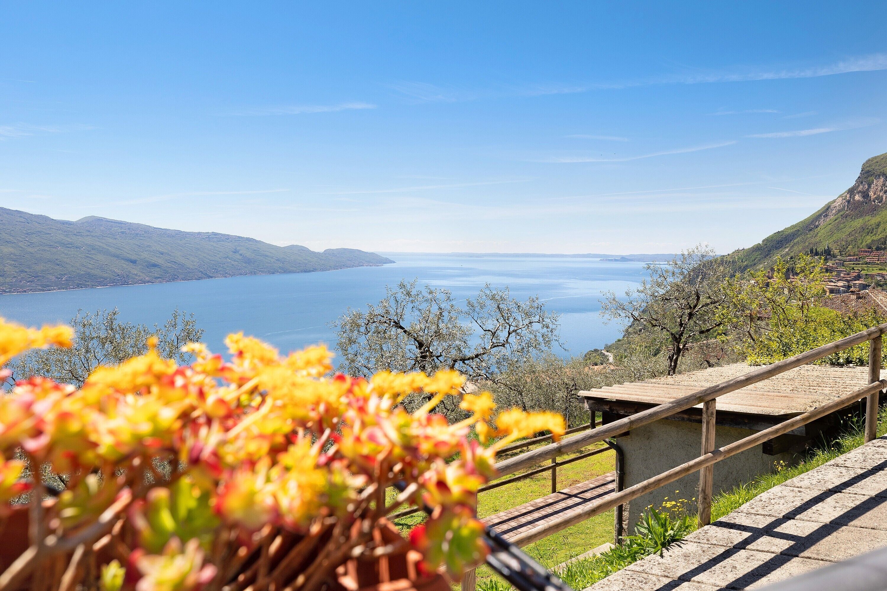 A scenic view of a lake with mountains in the background, a wooden deck, and a small building with a railing.