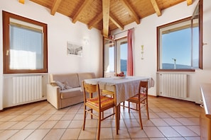 Habitació amb sostre de fusta, taula de dinar amb caires, sofà i finestrals amb cortines.
