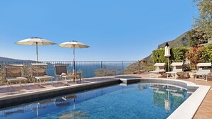 A swimming pool with lounge chairs and umbrellas, surrounded by a fence and a view of the sea. - Holiday Apartment 'Rustico Spagnol 2' with Lake View, Pool & Wi-Fi (Tignale)