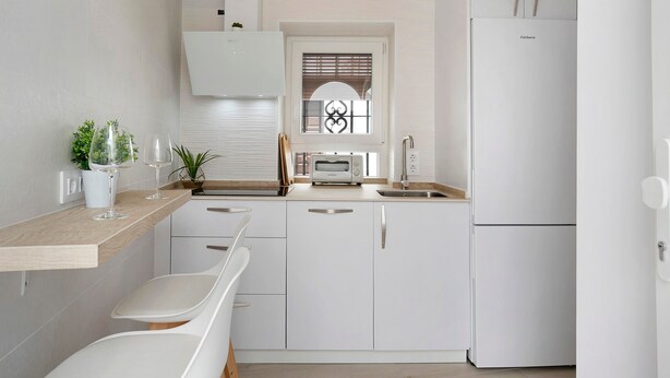 A modern kitchen with white cabinets, a built-in oven, a refrigerator, and a window with blinds. - Apartment "Cobarrubias" with Shared Terrace & Wi-Fi (Vejer)