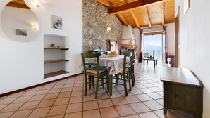 A dining area with a stone wall, wooden ceiling beams, and a view through a window. - Holiday Apartment 'Rustico Spagnol 4' with Lake View, Pool & Wi-Fi (Tignale)