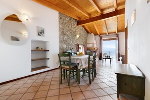 A dining area with a stone wall, wooden ceiling beams, and a view through a window.