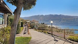 A paved pathway with a wooden railing, a small building, and a mountain backdrop. - Holiday Apartment 'Rustico Spagnol 4' with Lake View, Pool & Wi-Fi (Tignale)