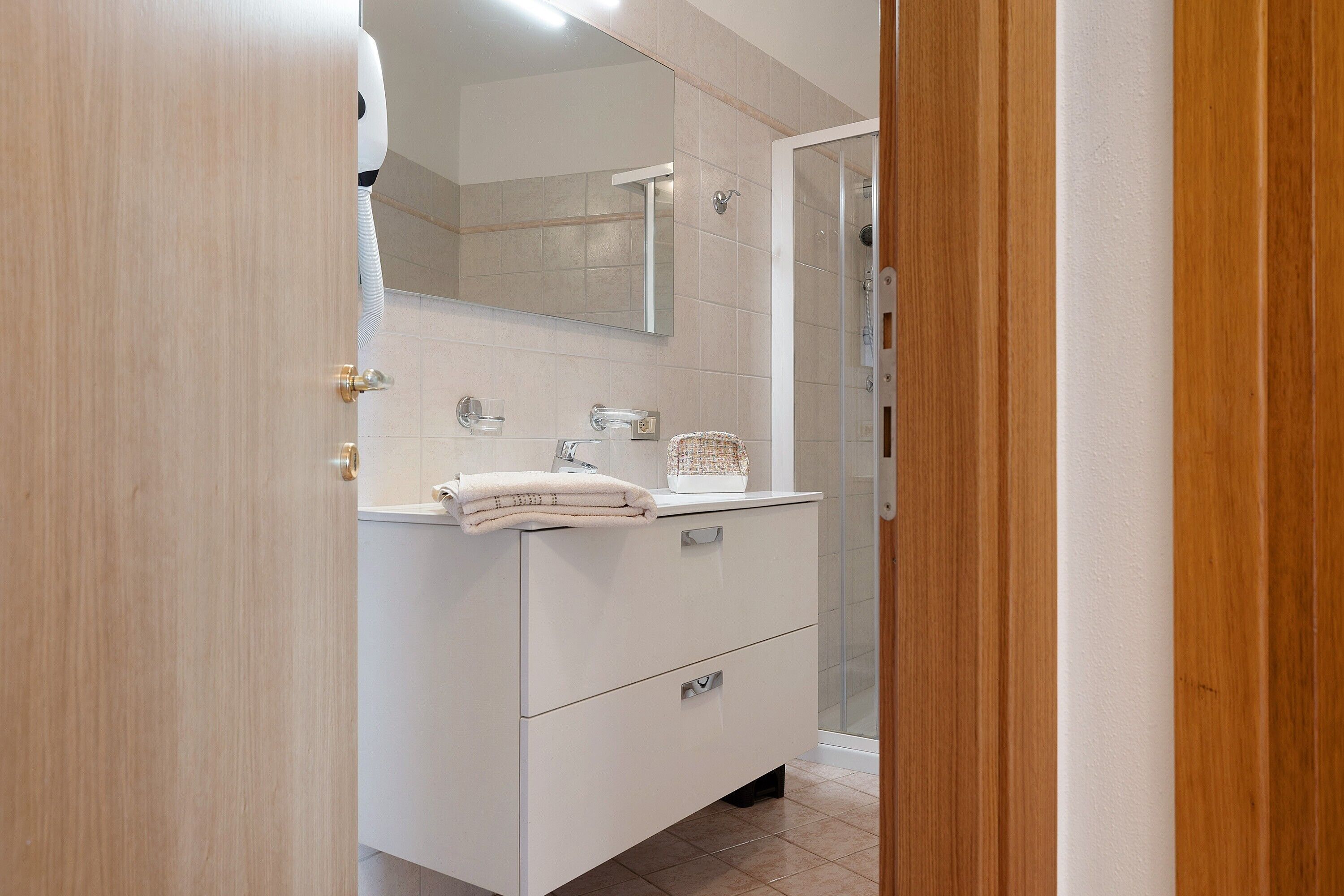 A bathroom with a white vanity, a mirror, a towel, and a shower area.