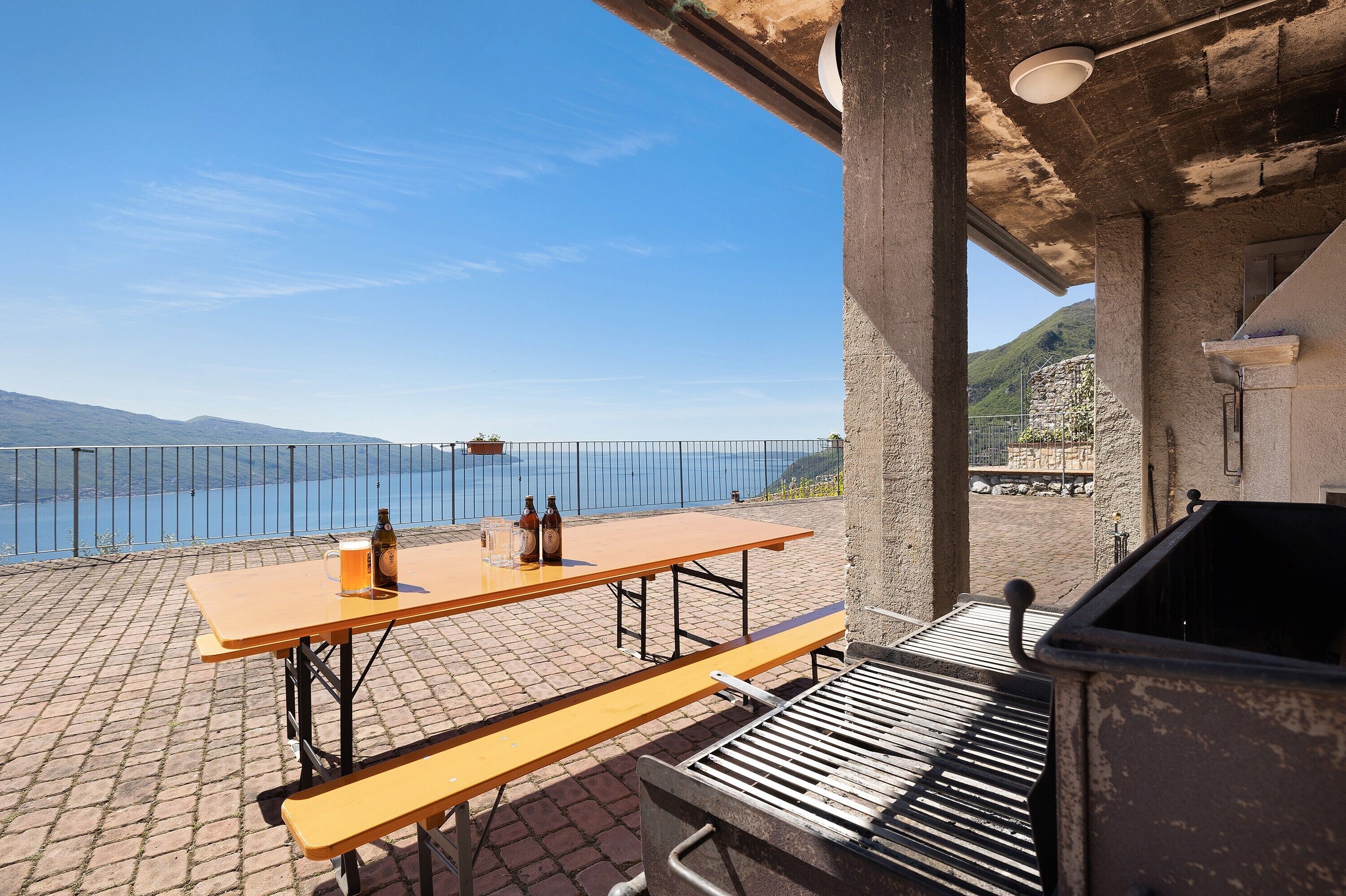 An outdoor patio with a table and benches, overlooking a body of water and mountains.