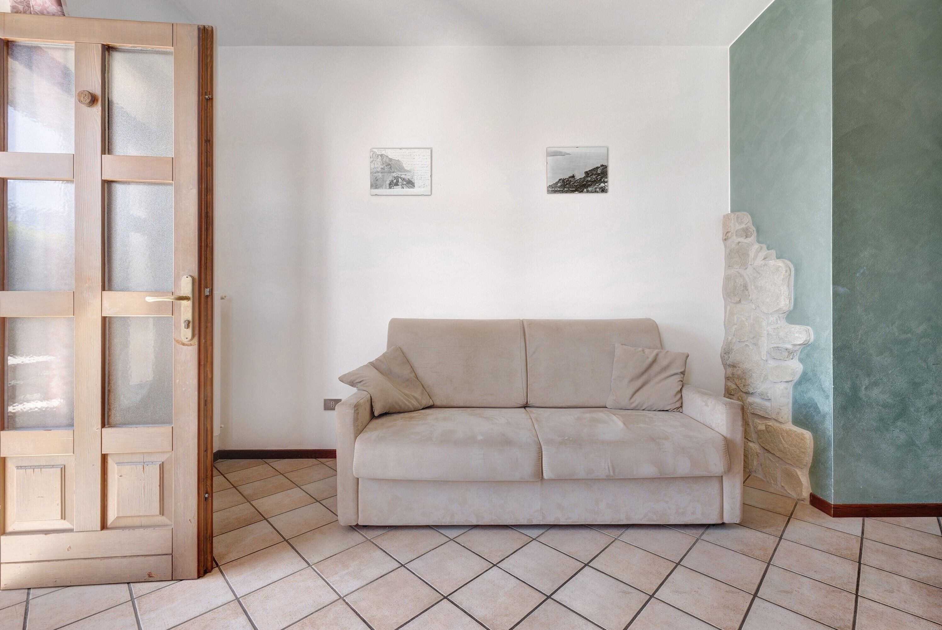 A room with a beige sofa, a wooden door with glass panels, and two framed pictures on the wall.