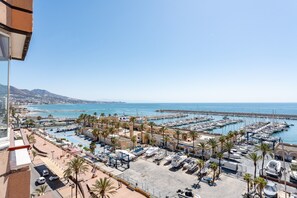 A marina with boats docked, palm trees, and a clear view of the sea.