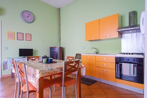 A kitchen with a dining table, chairs, a stove, and a clock on the wall.