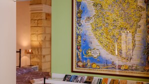 A framed map with a coastal region, a bed with a purple bedspread, a nightstand with a lamp, and a shelf with books. - Holiday Home 'I Colori di Civico 19' with Terraces & Wi-Fi (Galatina)