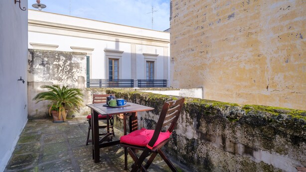 A small outdoor patio with a table and chairs, a potted plant, and a building in the background. - Holiday Home 'I Colori di Civico 19' with Terraces & Wi-Fi (Galatina)