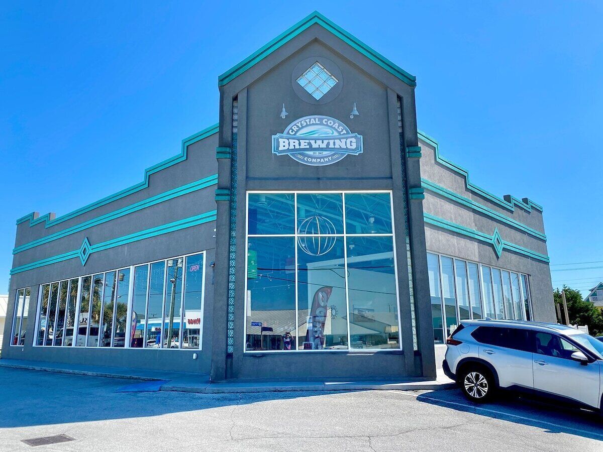 A building with a large glass facade, a sign reading 'Crystal Coast Brewing Company,' and a car parked in front.