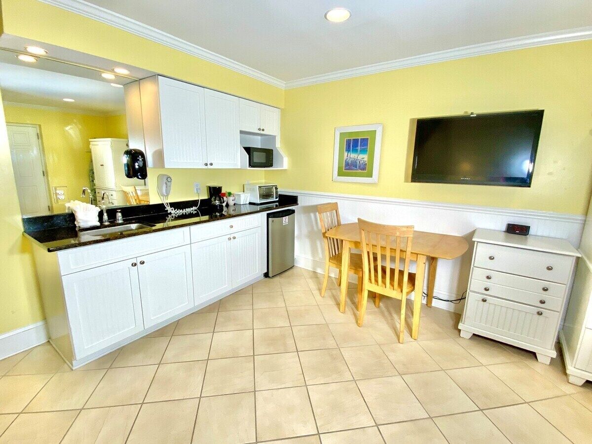 A kitchen with white cabinets, a dining table with chairs, a microwave, and a television mounted on the wall.