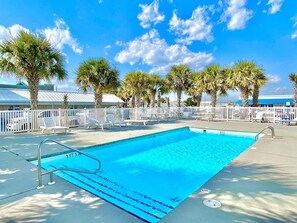 Une piscine entourée d’une clôture blanche, avec des palmiers et un ciel bleu azur.