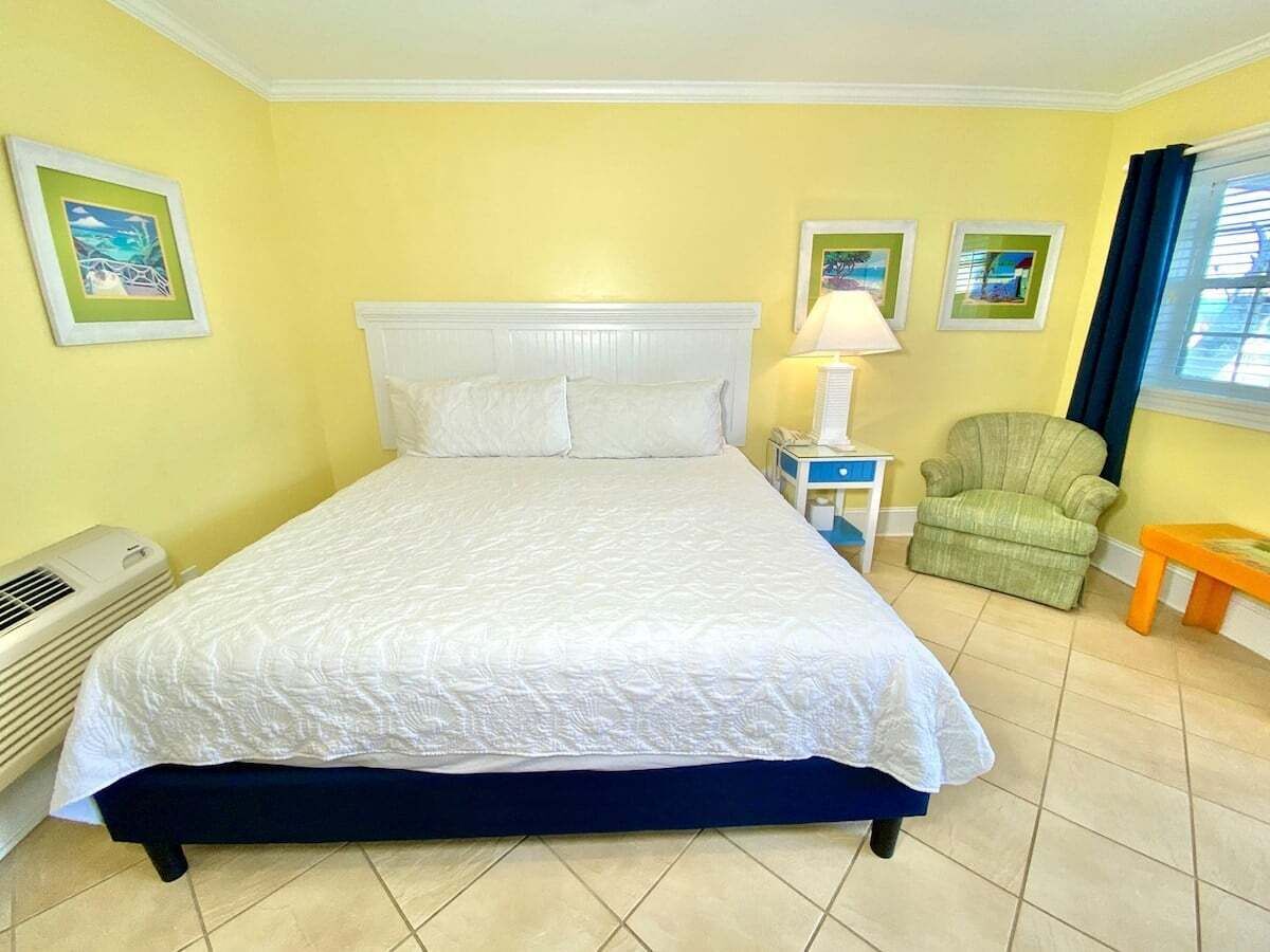 Una cama con cabecera blanca, una lámpara de noche, una silla verde y una mesita.
