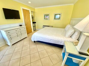 Une chambre d’hôtel avec un lit, une commode, un bureau avec une lampe, une télévision et une porte.