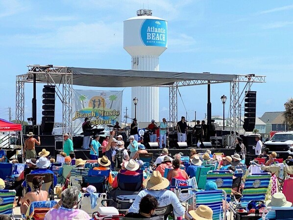 A stage with a crowd of people, a water tower, and a beach music festival banner.